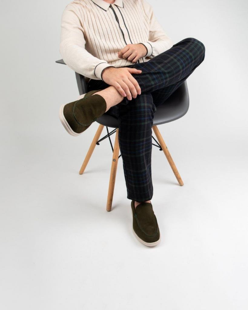 Hombre sentado con mocasines de gamuza verde combinados con pantalón a cuadros en un estilo casual elegante