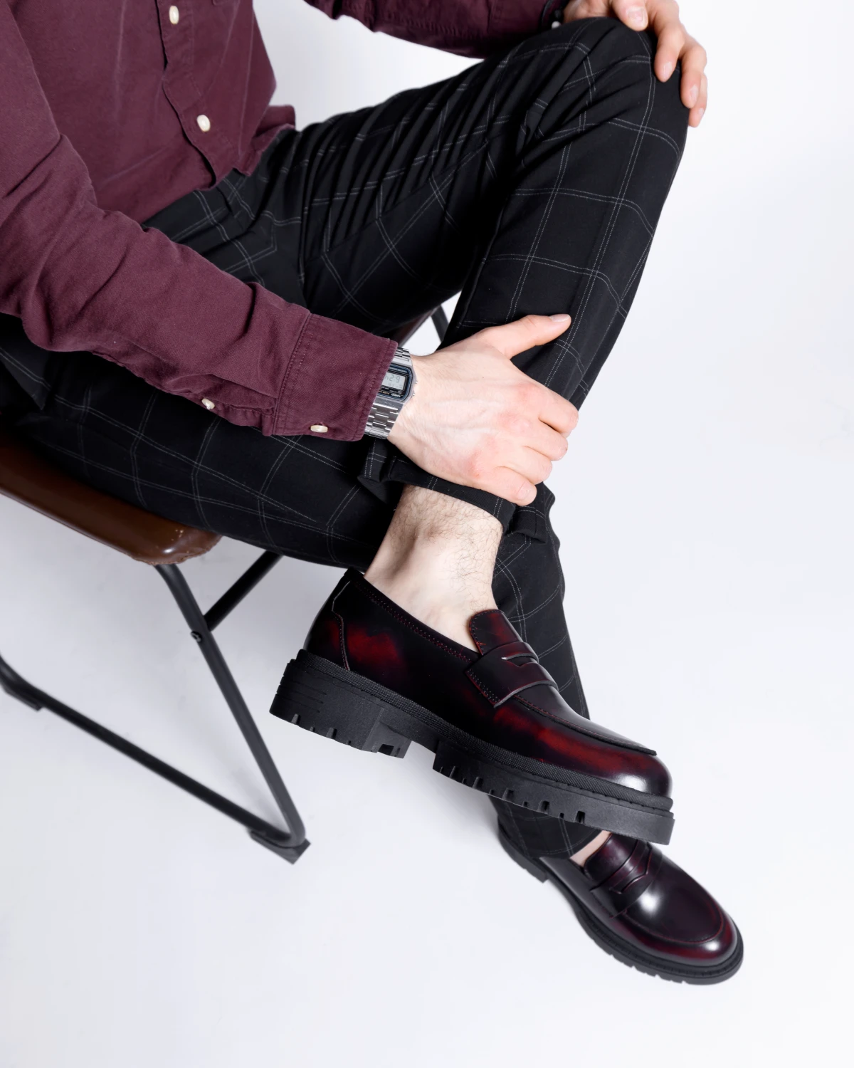 Hombre usando mocasines color vino con pantalón negro de cuadros y camisa en tono vino.