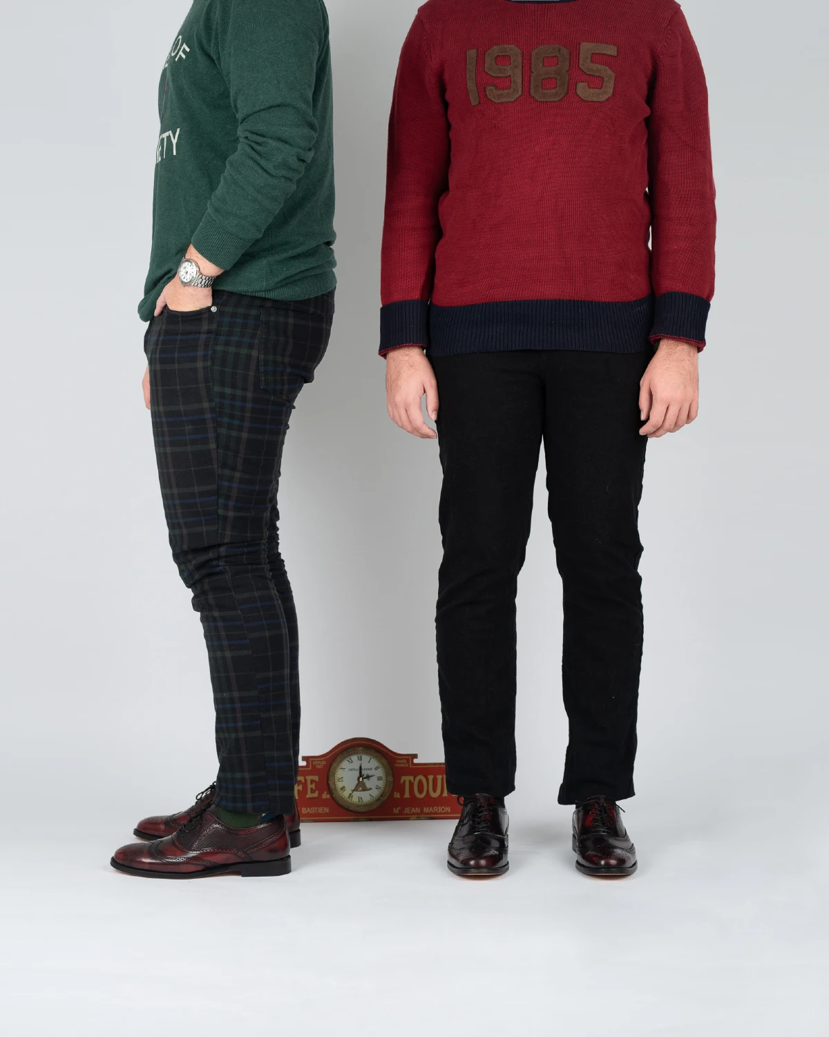 Dos hombres combinan zapatos color vino con pantalón negro, camisa roja y prendas verdes.