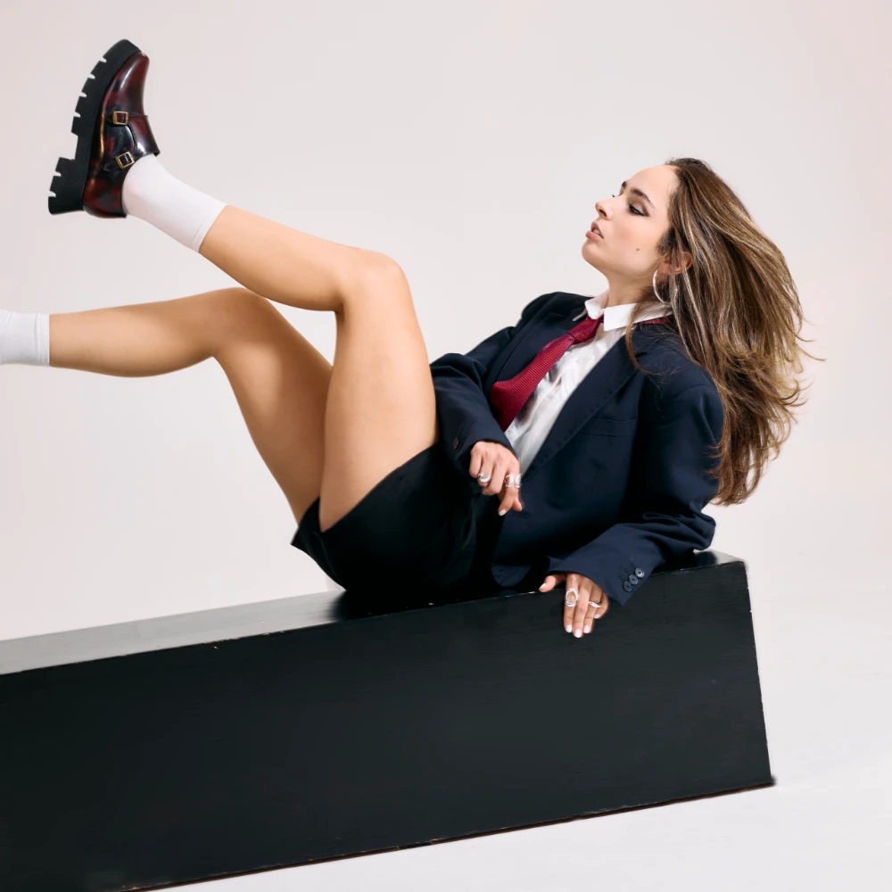 Zapato monkstrap para mujer en piel vino con doble hebilla metálica y suela gruesa negra, mostrado con la pierna elevada.