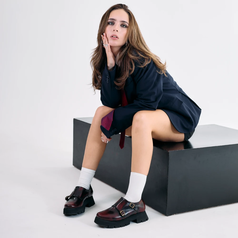 Zapatos color vino para mujer en piel vacuno con doble hebilla y suela chunky negra, usados con calcetines blancos.