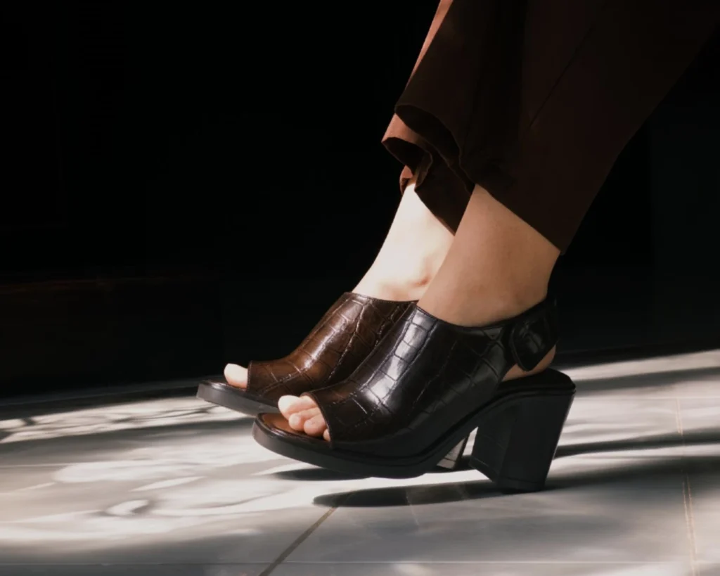 Sandalia de tacón bloque café con grabado tipo cocodrilo y abertura discreta en la punta, combinada con pantalón de vestir marrón. Un calzado formal y elegante ideal para la oficina o eventos semi-formales.