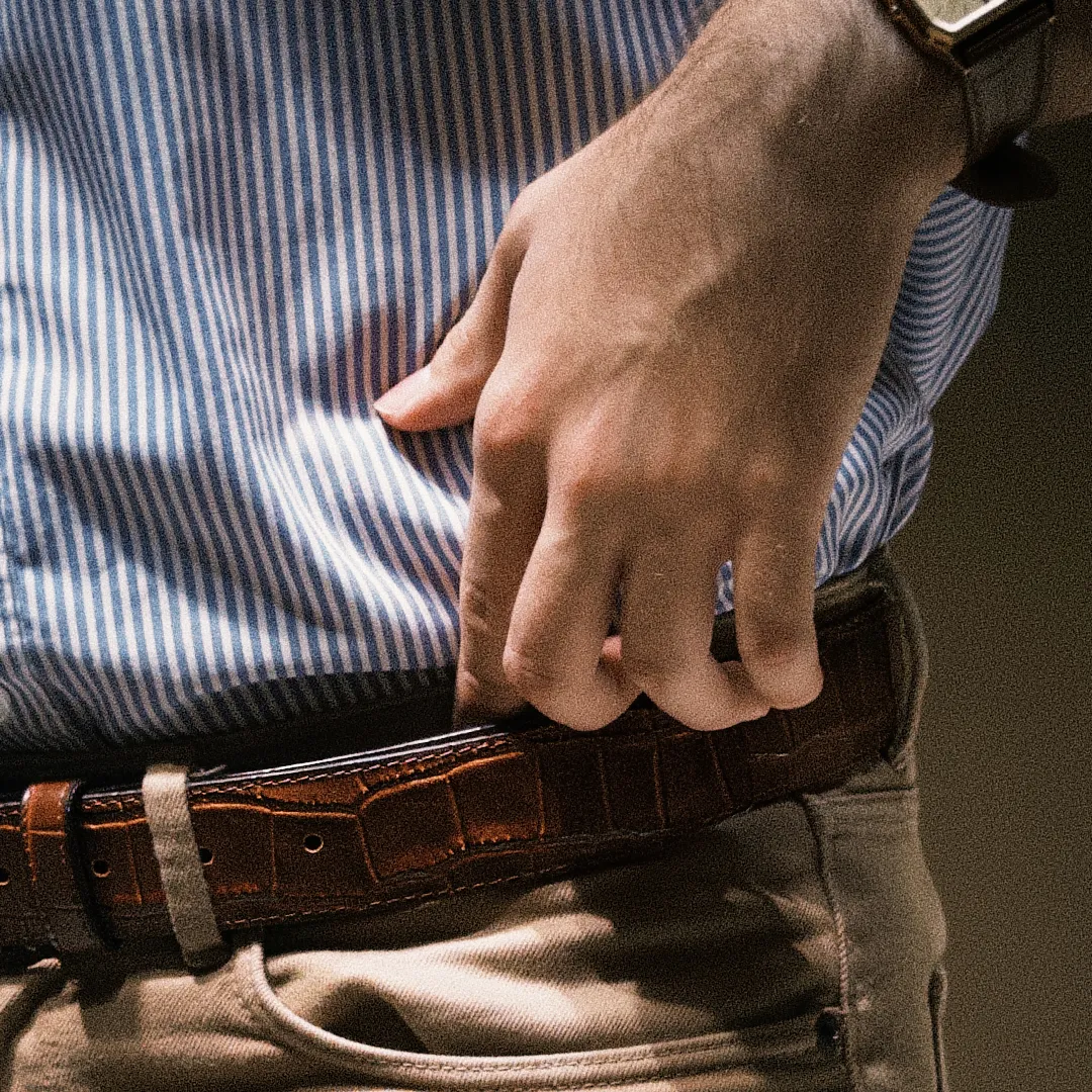 Hombre usando cinturón café de piel vacuno con grabado cocodrilo en pantalón de tono neutro
