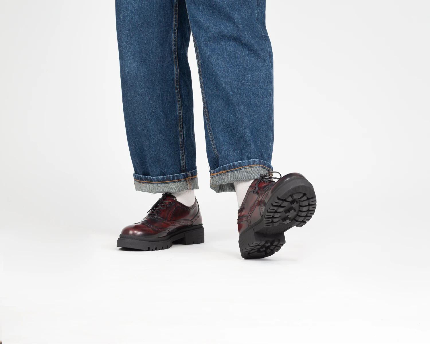 Zapato moderno de vestir tipo brogue color vino con suela track y jeans, imagen destacada sobre las tendencias de calzado para hombre.