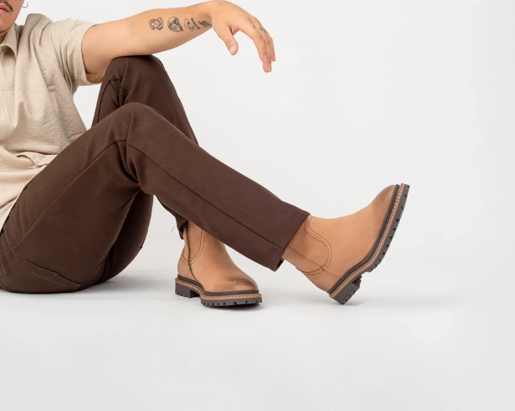 Hombre sentado usando botas sin agujetas estilo Roper en piel nobuck café claro, con suela dentada.